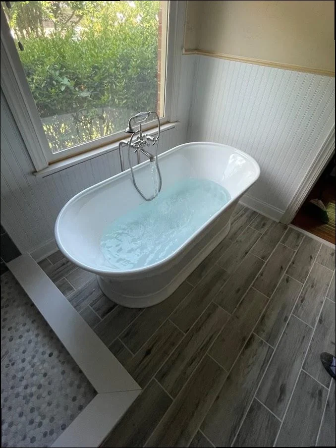 Freestanding luxury tub installed with wood-look tile floors and garden window by Sandy Springs Plumbing